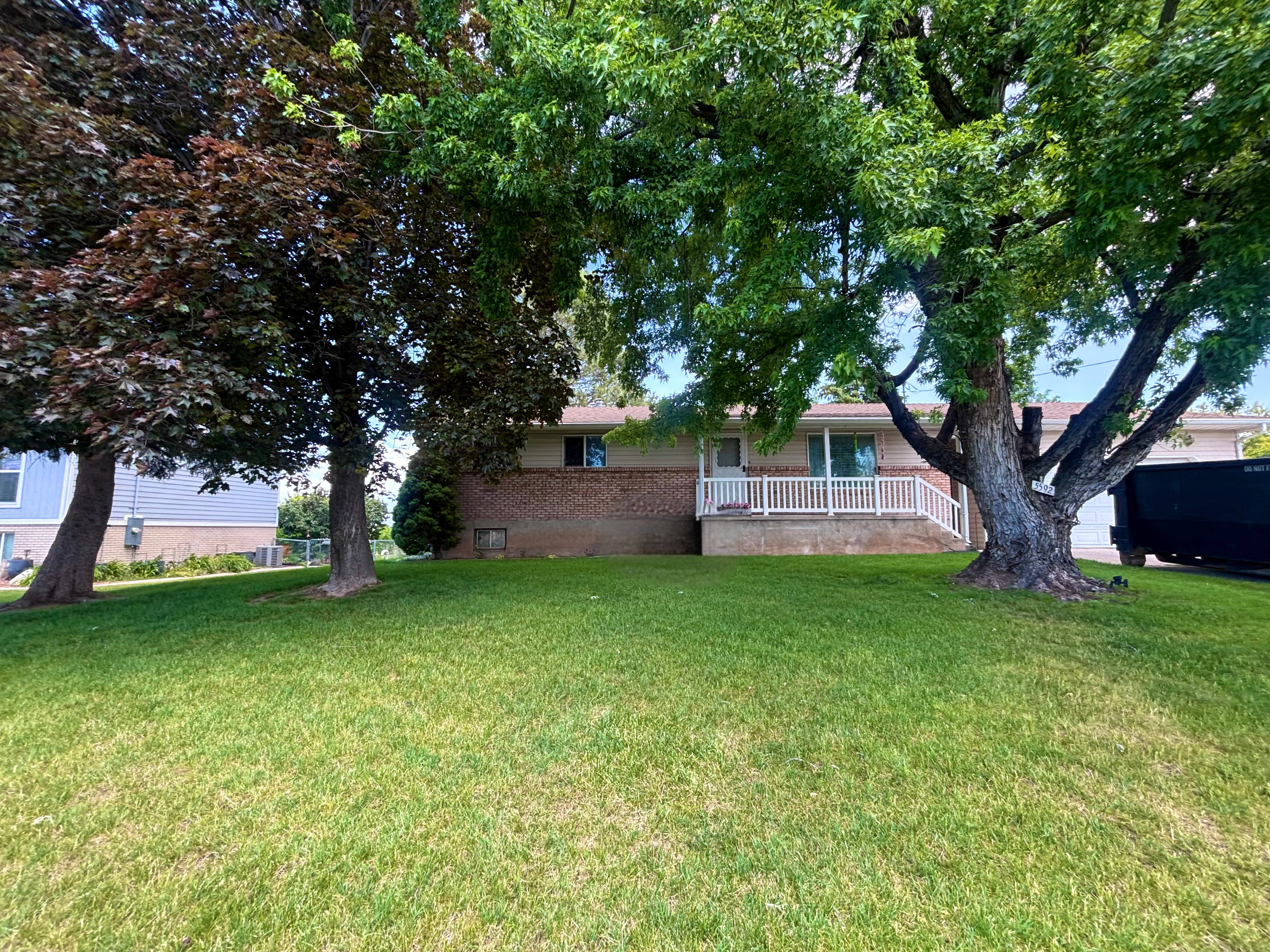 Front yard with a manicured lawn, established mature trees, and a red brick facade