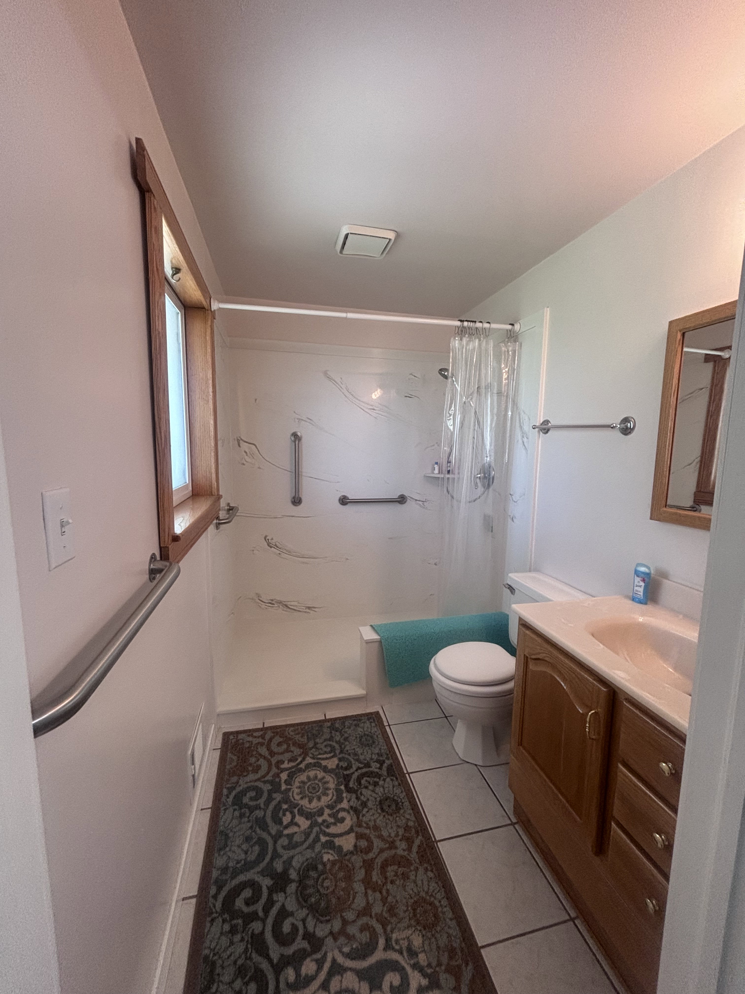 Bathroom featuring a window with wood trim, ceramic tile flooring, a wood-finish vanity with an integrated sink, and a shower-over-tub combination with grab bars