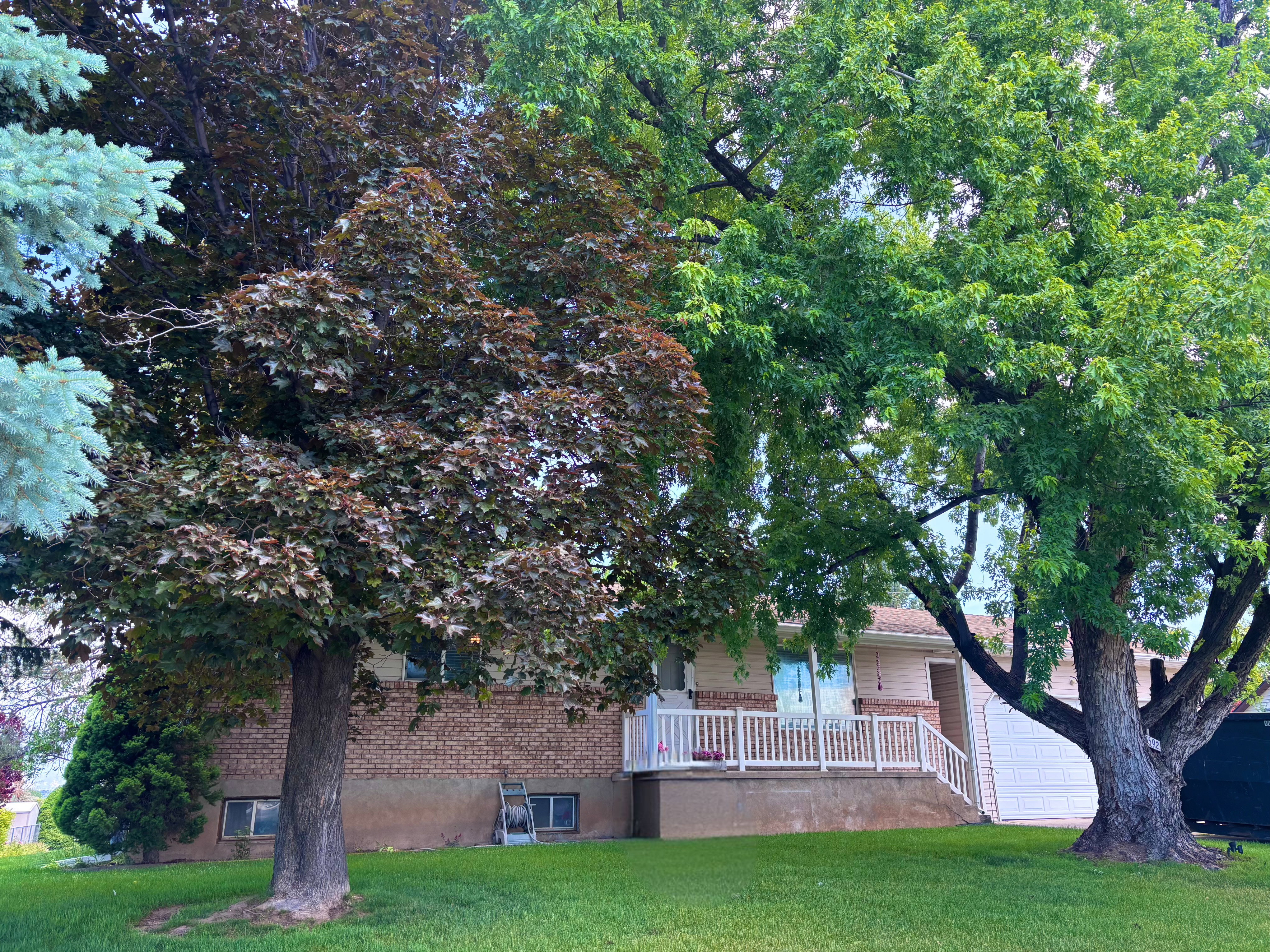 Exterior featuring a brick facade, white porch railing, and an expansive front lawn