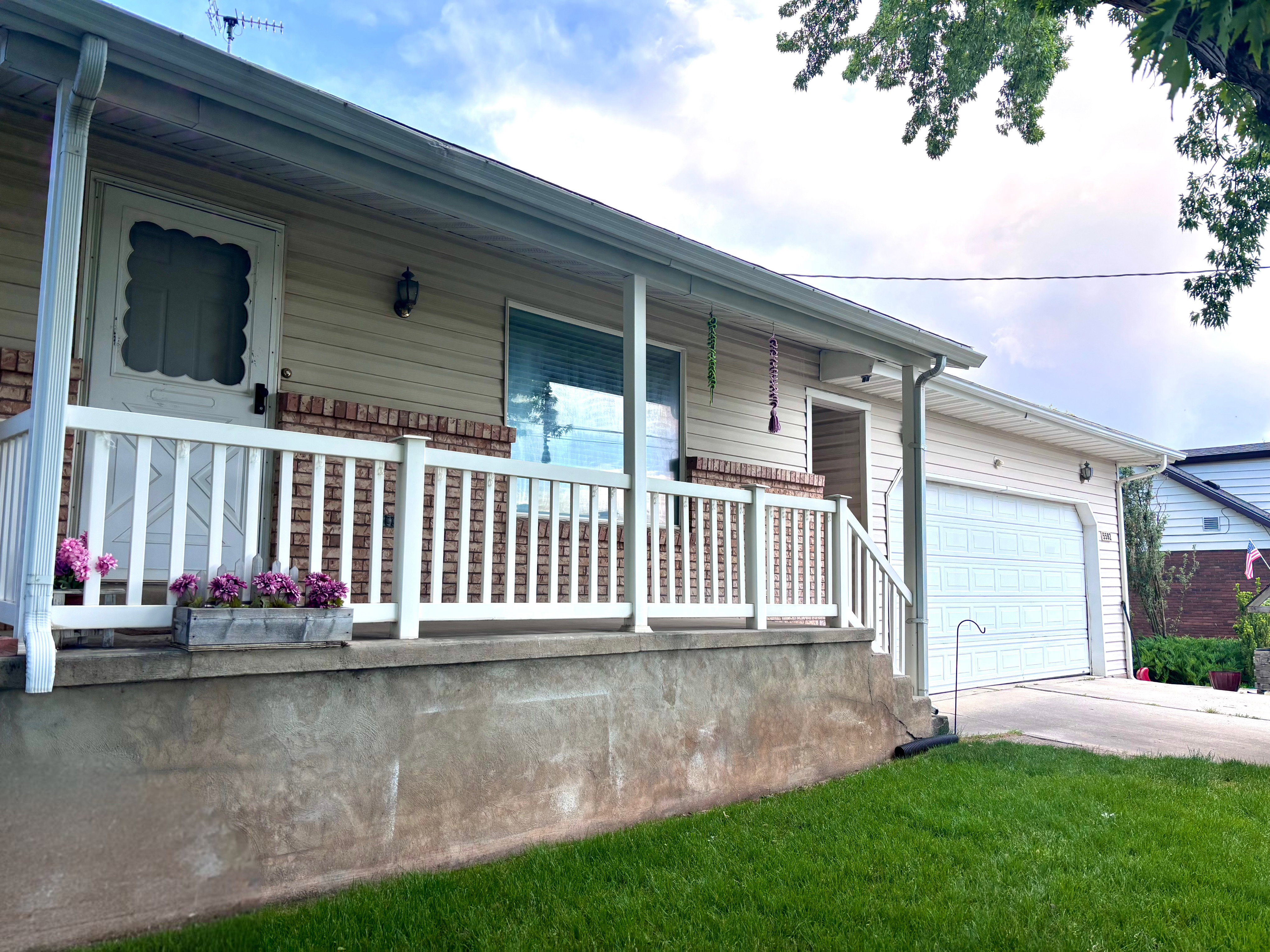 Front exterior featuring a white porch railing, brick facade accents, and light-colored siding