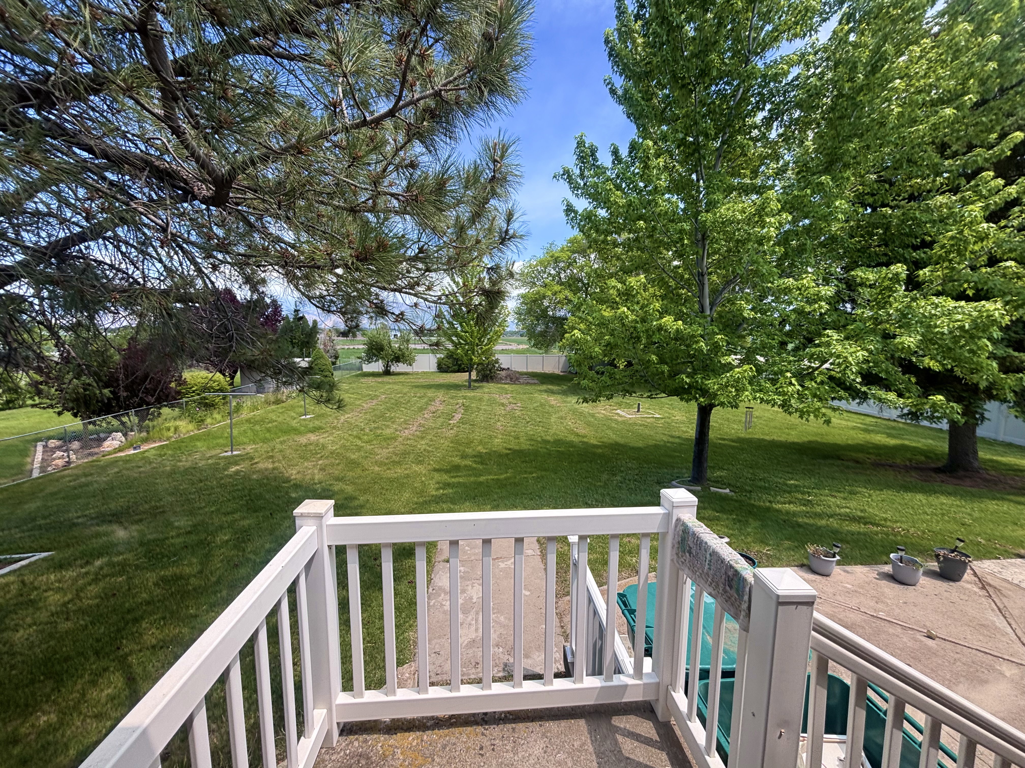 Expansive green space featuring mature trees and a concrete patio with white railing