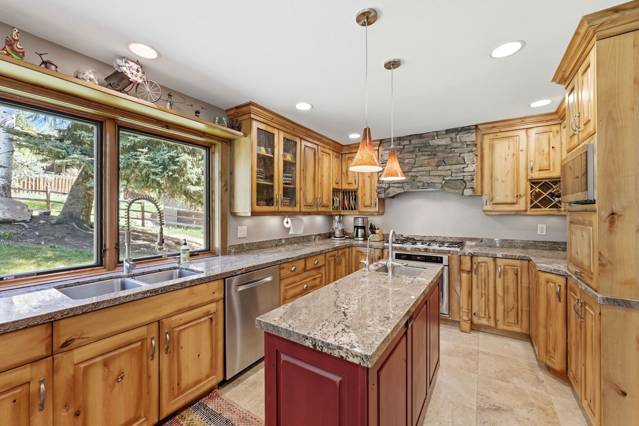 Gourmet kitchen featuring custom wood cabinetry, stone countertops, a large center island with pendant lighting, a built-in wine rack, and a stone-clad range hood