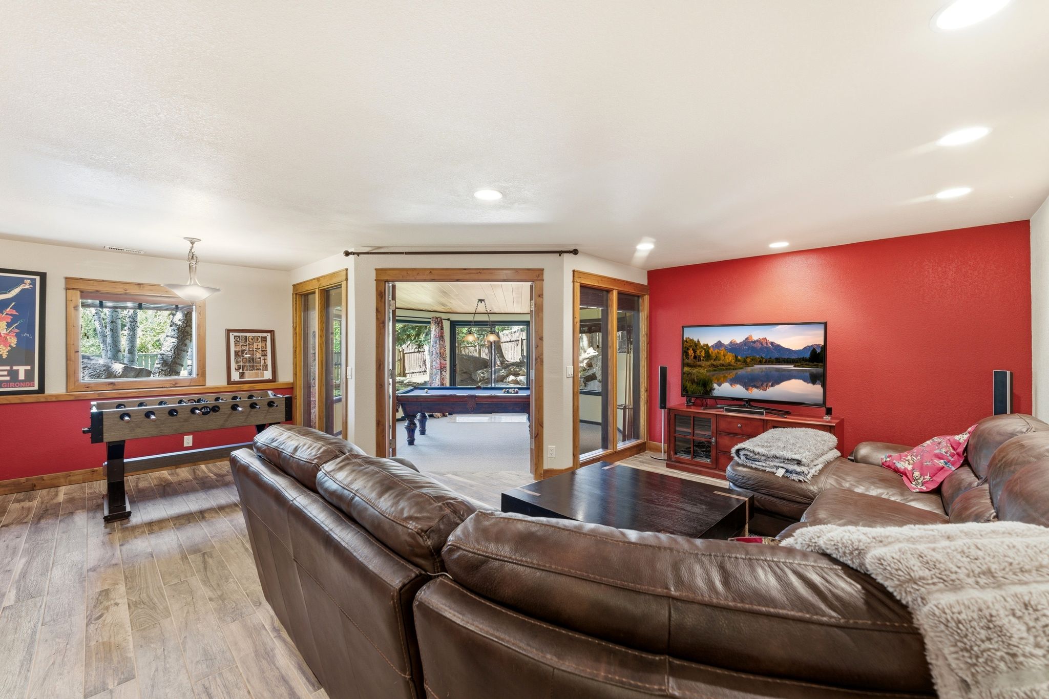 Spacious entertainment area featuring wood-finish flooring, a vibrant accent wall, recessed lighting, and large windows with natural wood trim