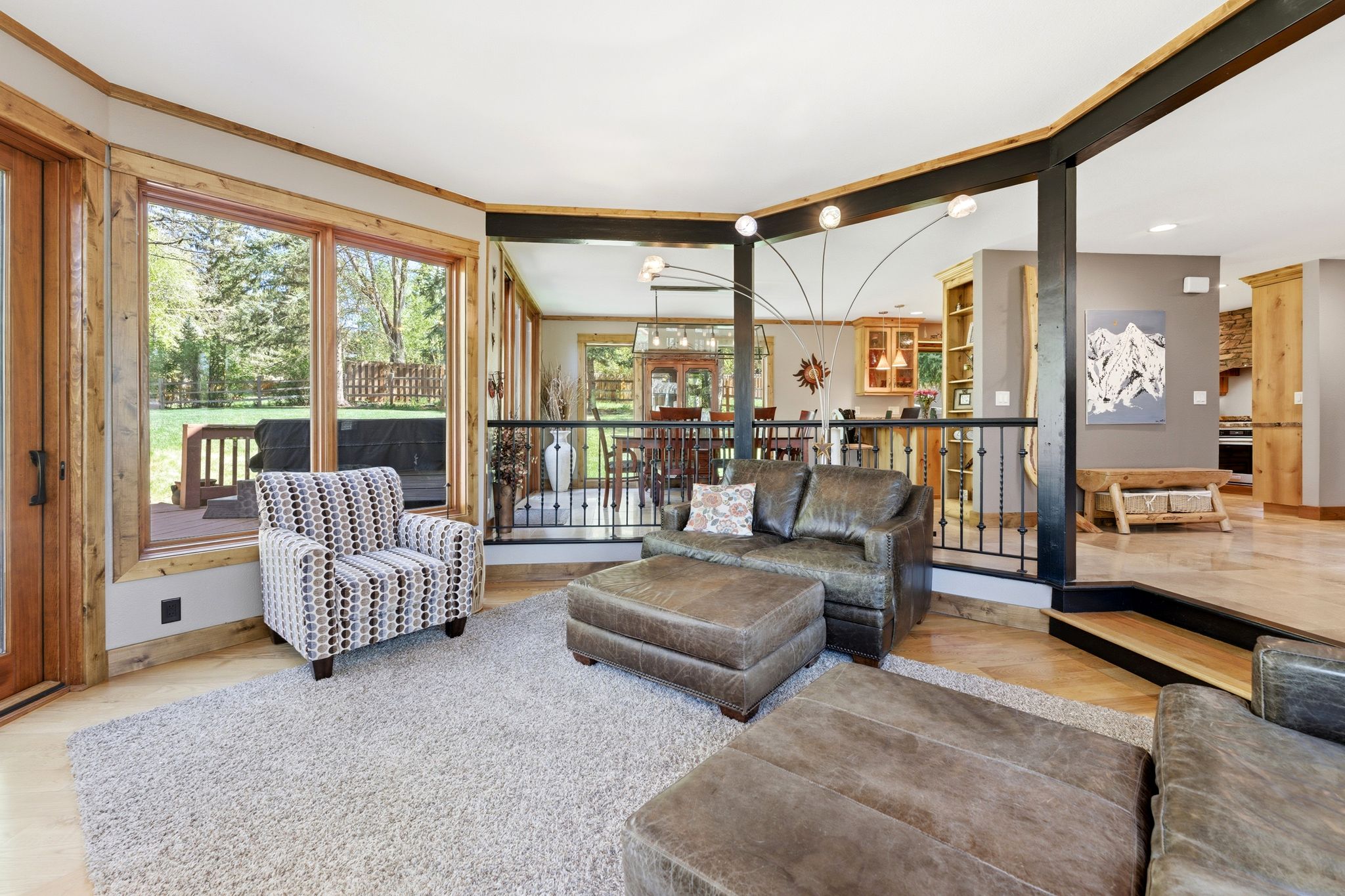 Open-concept living area featuring light wood-finish flooring, a neutral-toned area rug, and a perimeter of natural wood trim