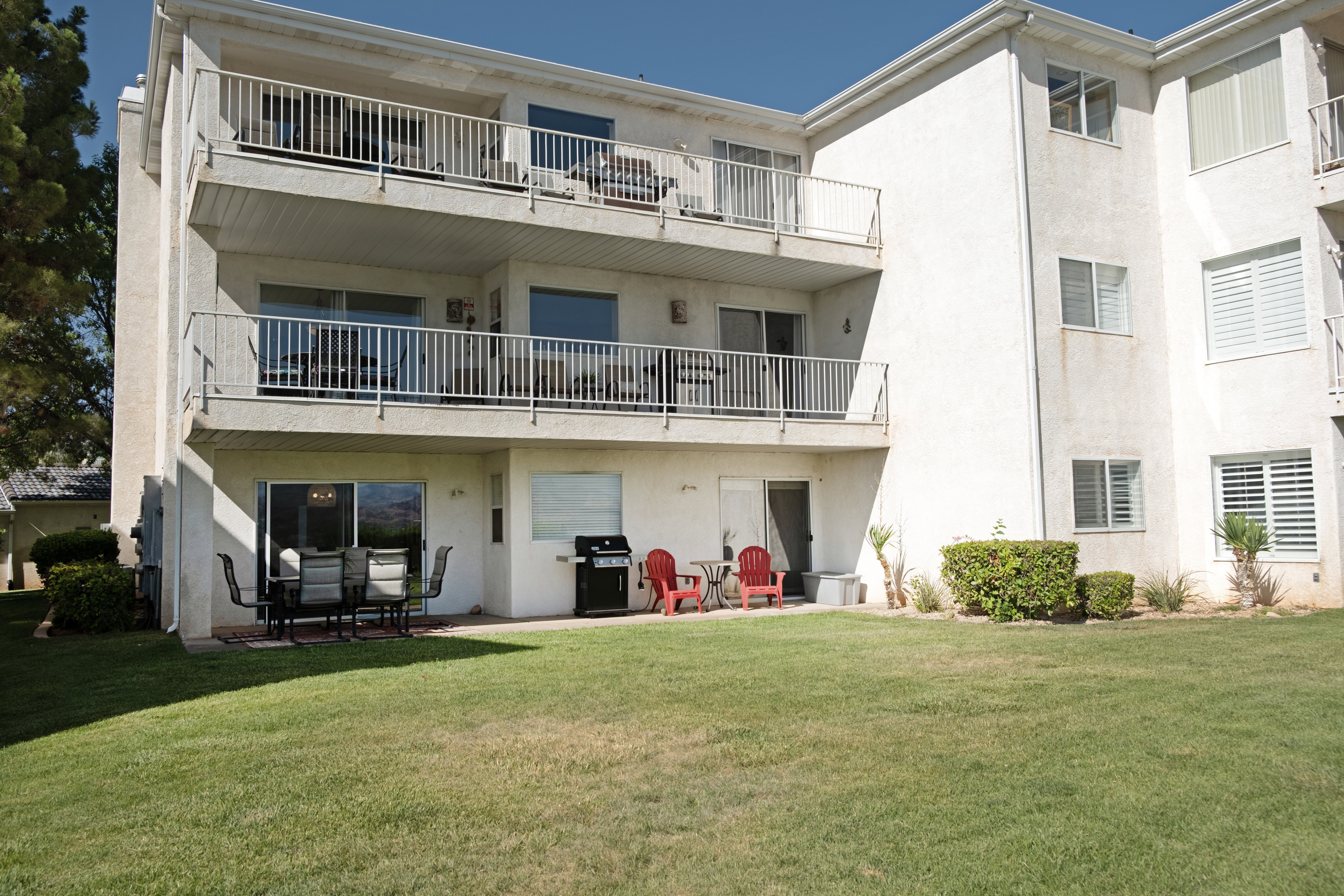Multi-story building featuring private balconies, ground-level patio space, sliding glass doors, and manicured lawn areas
