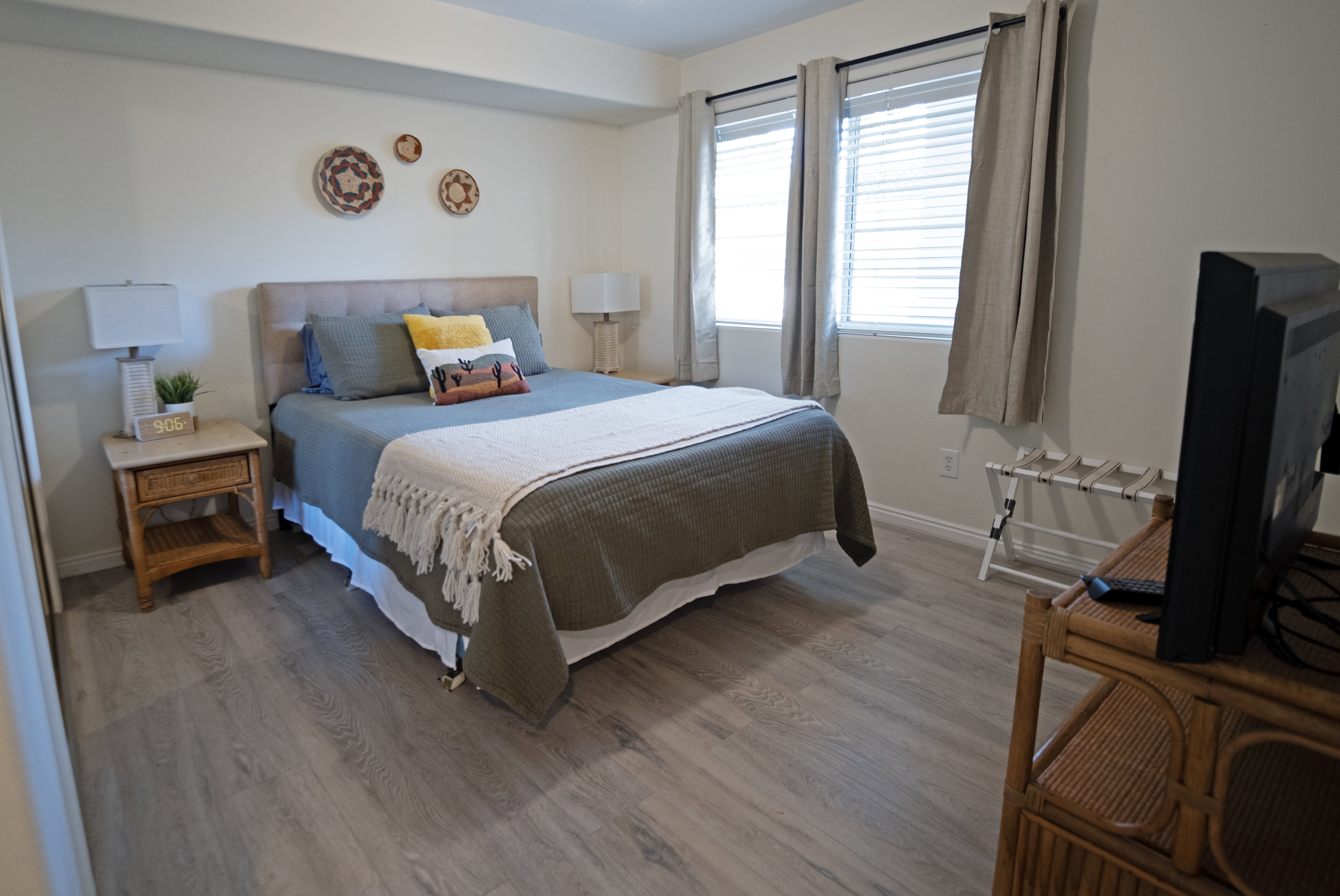 Bedroom featuring wood-finish flooring, neutral wall tones, and two windows with blinds and drapes