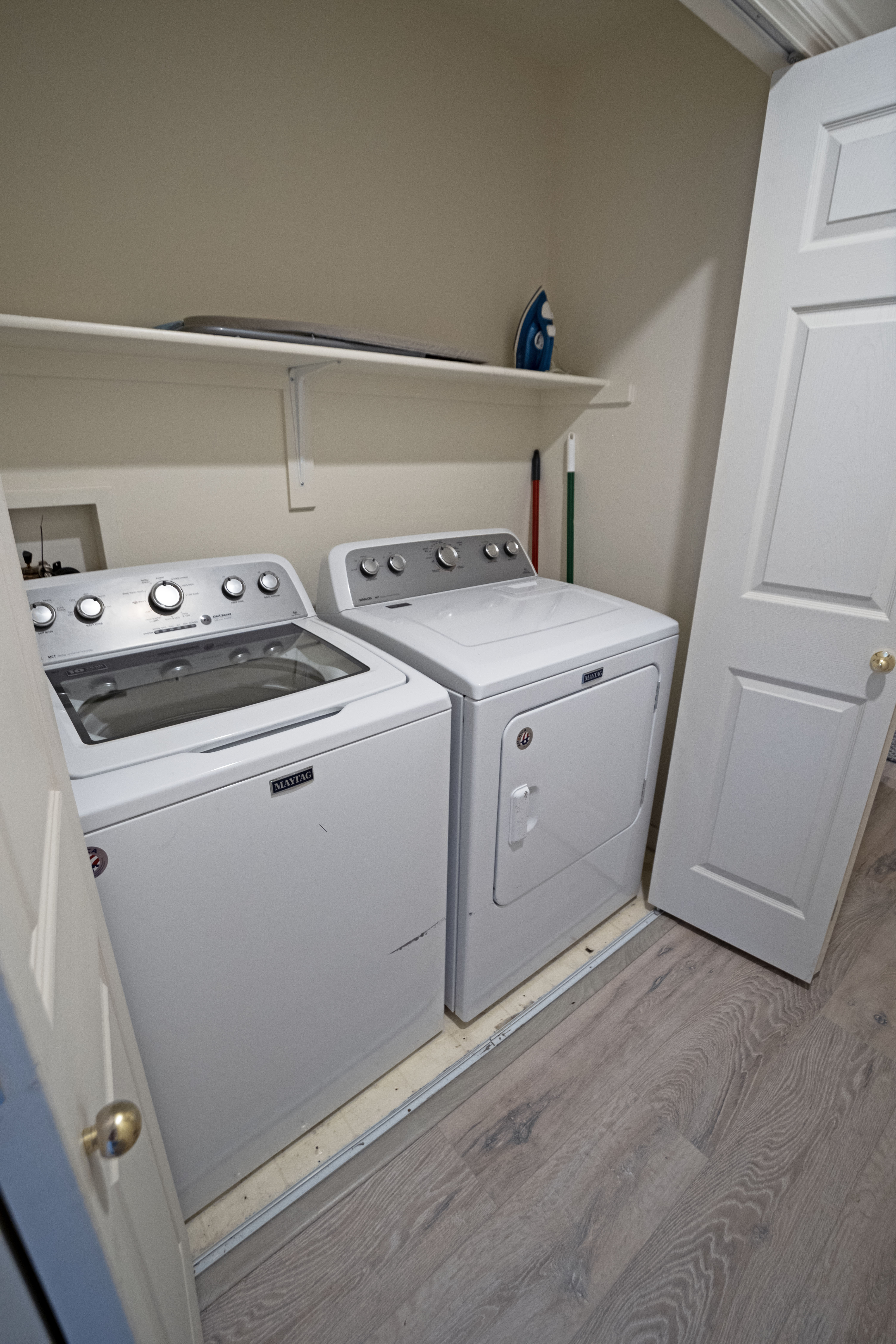 Dedicated laundry area featuring a washer and dryer, wood-finish flooring, a wall-mounted storage shelf, and a panel door with a brass knob