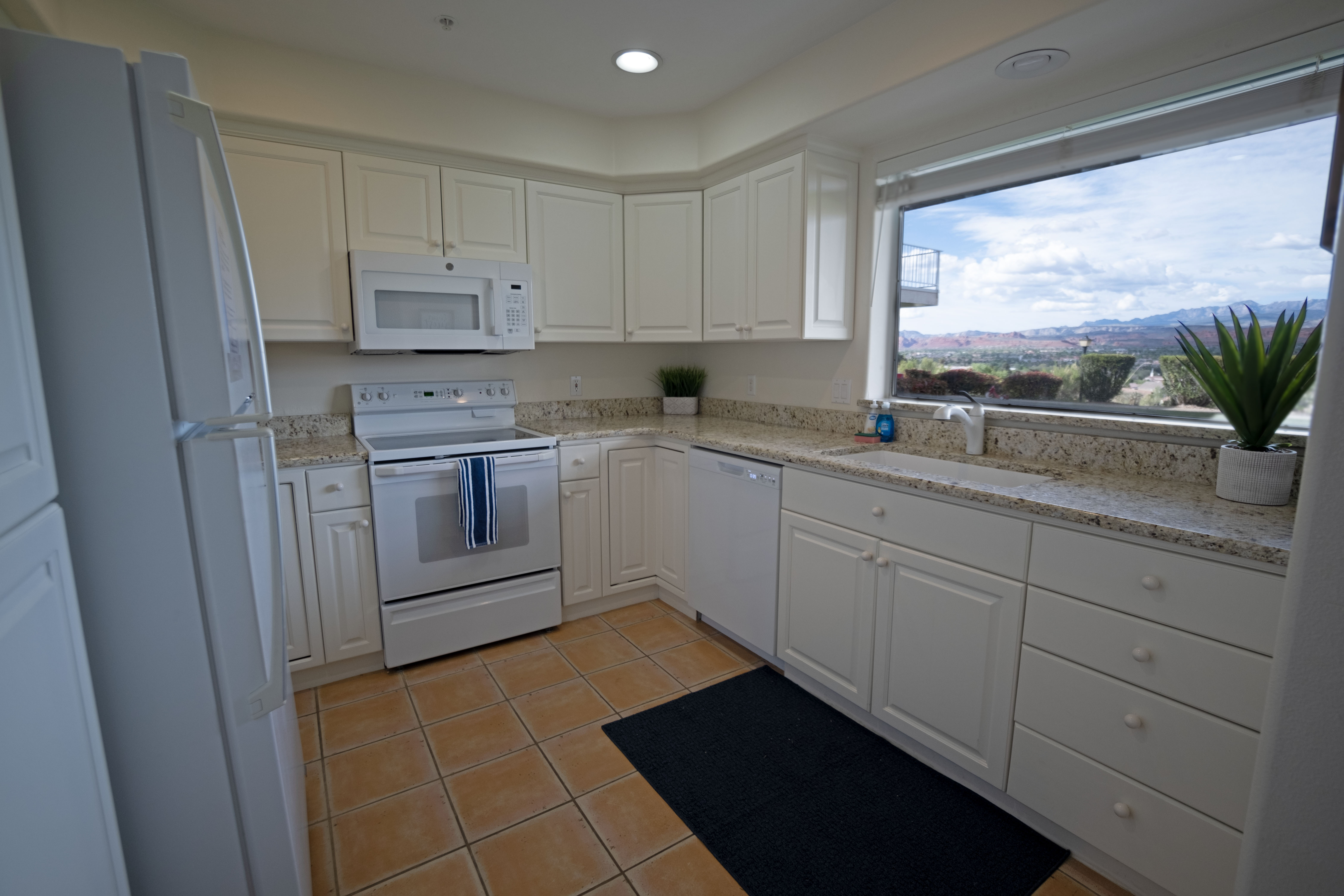 Kitchen featuring a large picture window, white cabinetry with round knobs, light granite countertops, and tile flooring