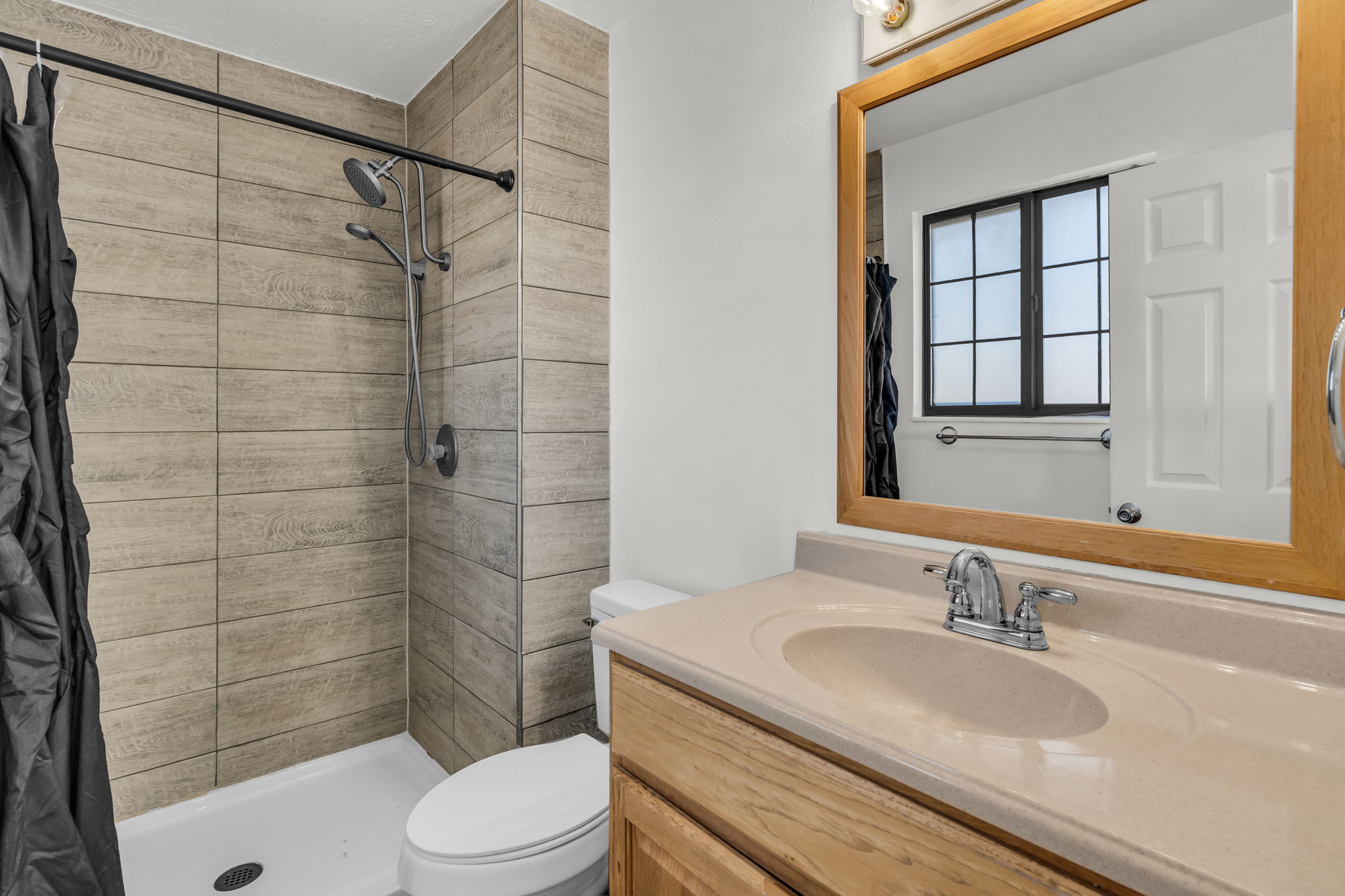 Bathroom featuring a walk-in shower with wood-finish tile surround, chrome shower fixtures, and a white shower pan
