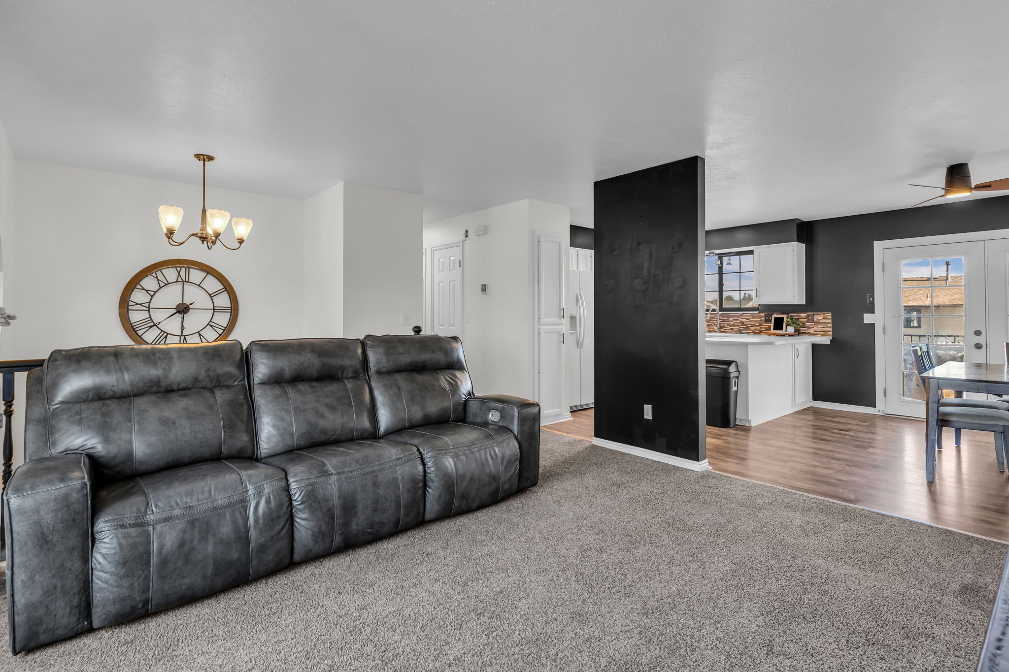 Carpeted living area with a dark accent wall, featuring a bronze chandelier, wood-finish flooring, white cabinetry, and double glass-paneled doors