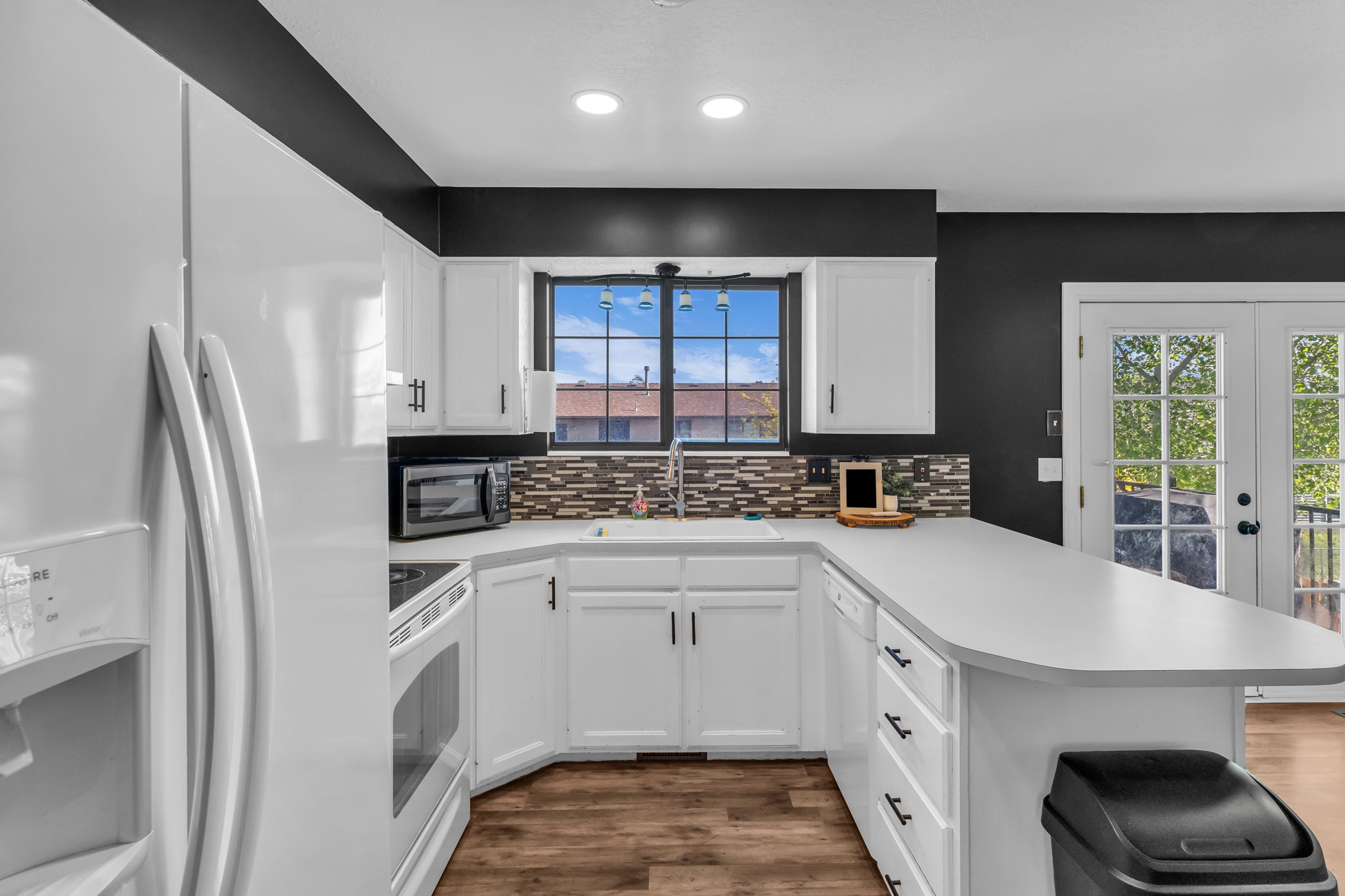 Kitchen featuring white cabinetry, light countertops, mosaic tile backsplash, black walls, and wood-finish flooring