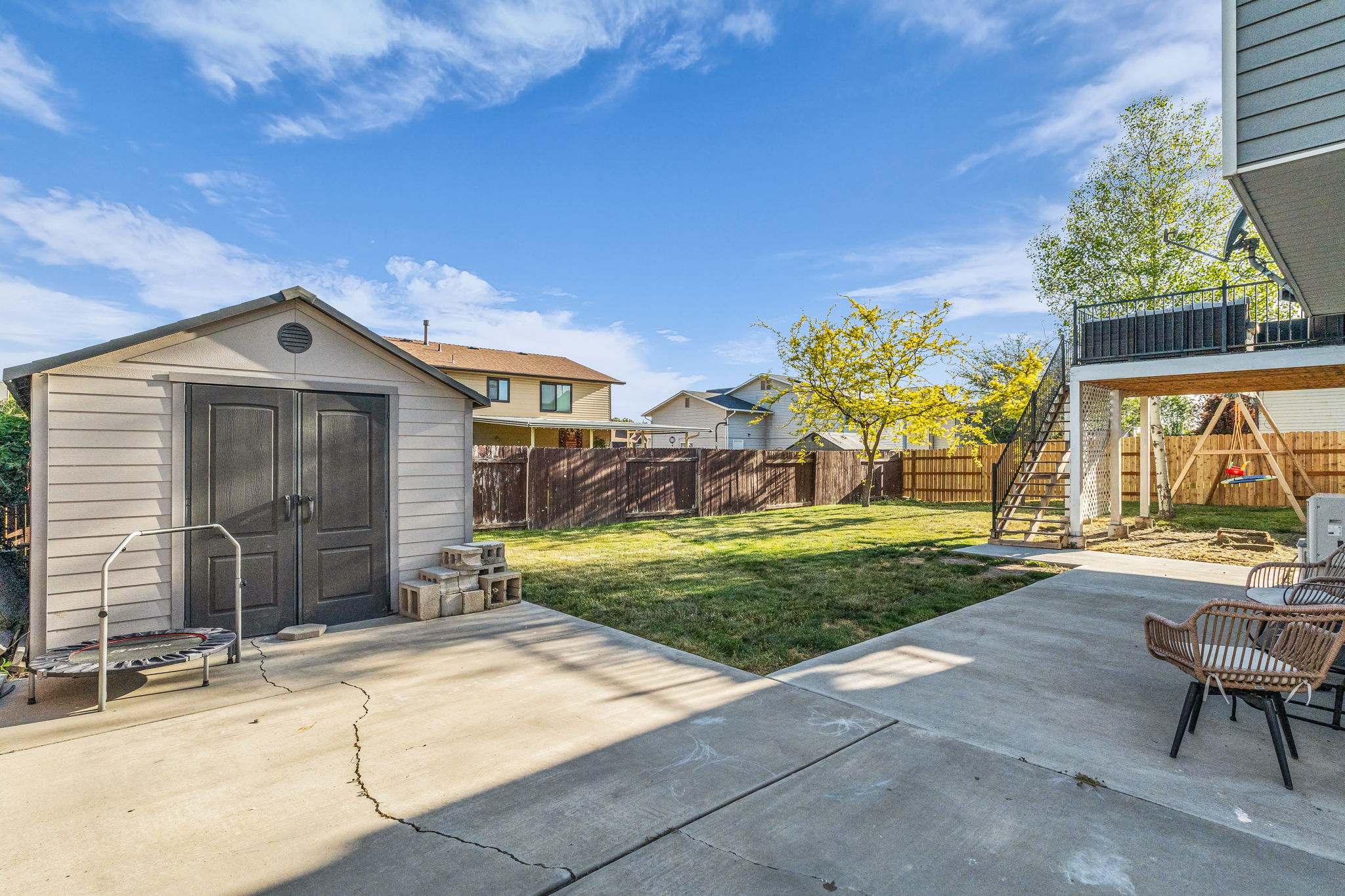 Expansive backyard featuring a concrete patio, a detached storage shed with double doors, and a wood privacy fence
