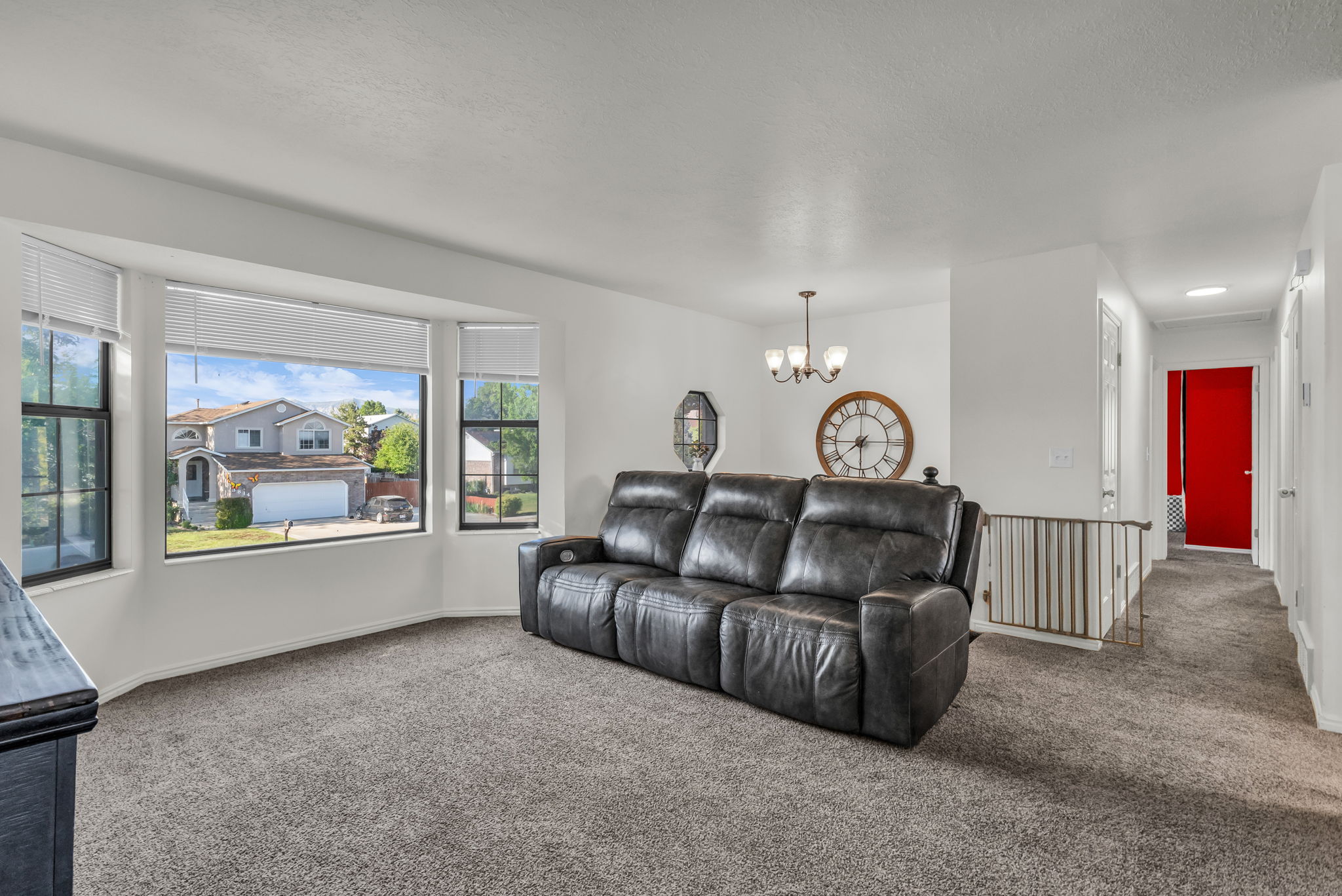 Living area featuring a bay window with multiple panes, carpet flooring, a white ceiling, and a hallway entrance