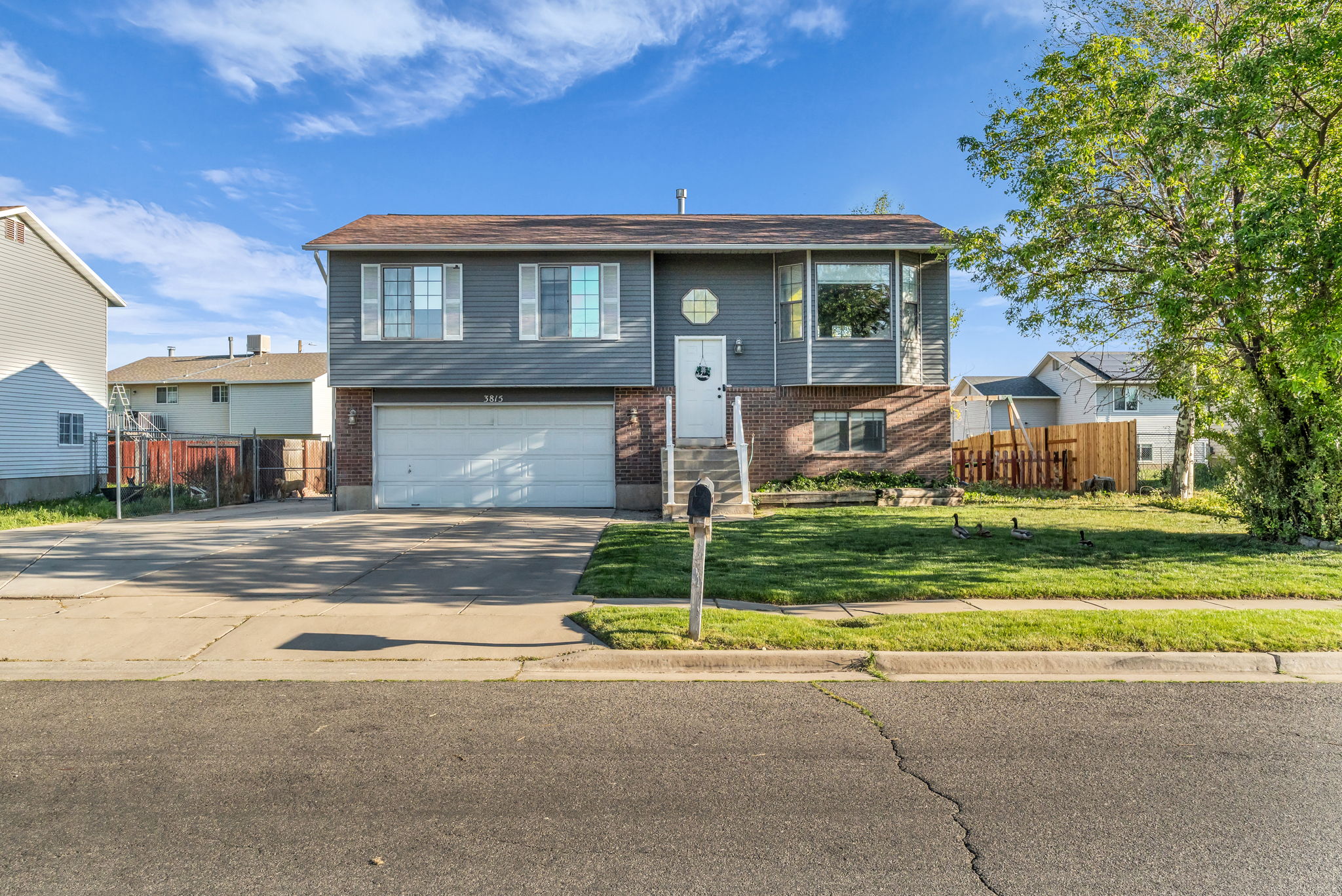 Split-level residence featuring a two-car garage, brick and siding exterior, front lawn, and mature trees