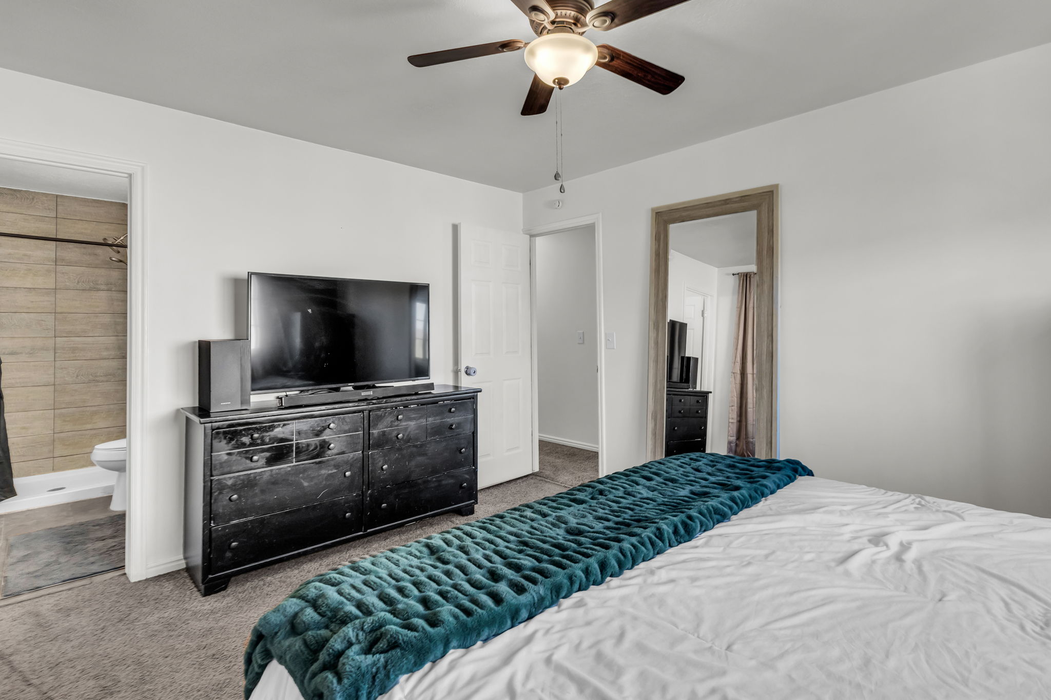 Carpeted bedroom with a ceiling fan light fixture, white walls, and a full-length framed mirror