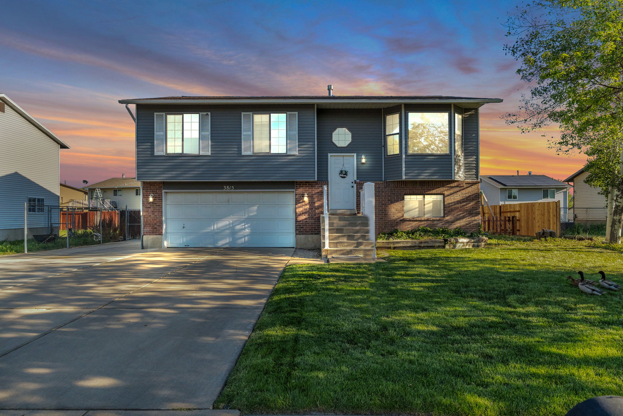 Split-level residence featuring a two-car garage, gray siding, and brick accents