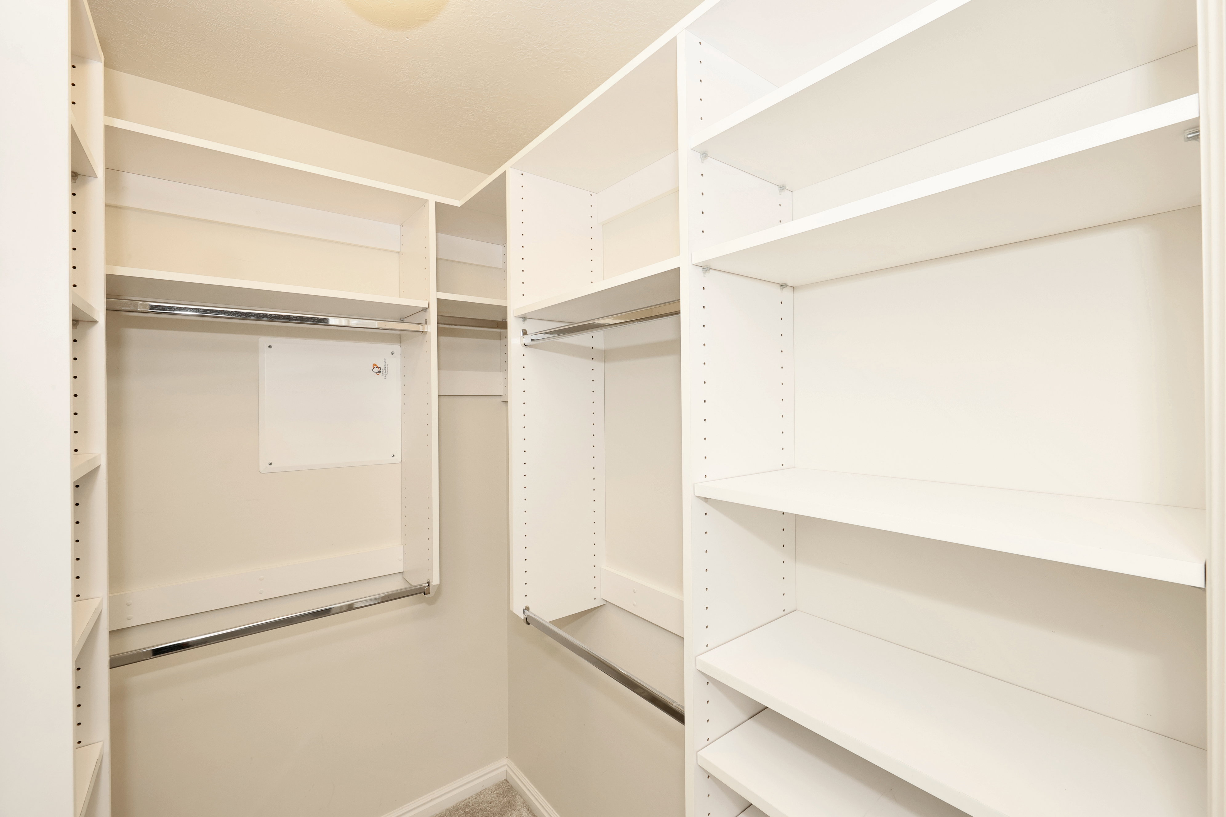 Walk-in closet featuring custom white shelving, multiple hanging rods, and light-toned carpeting