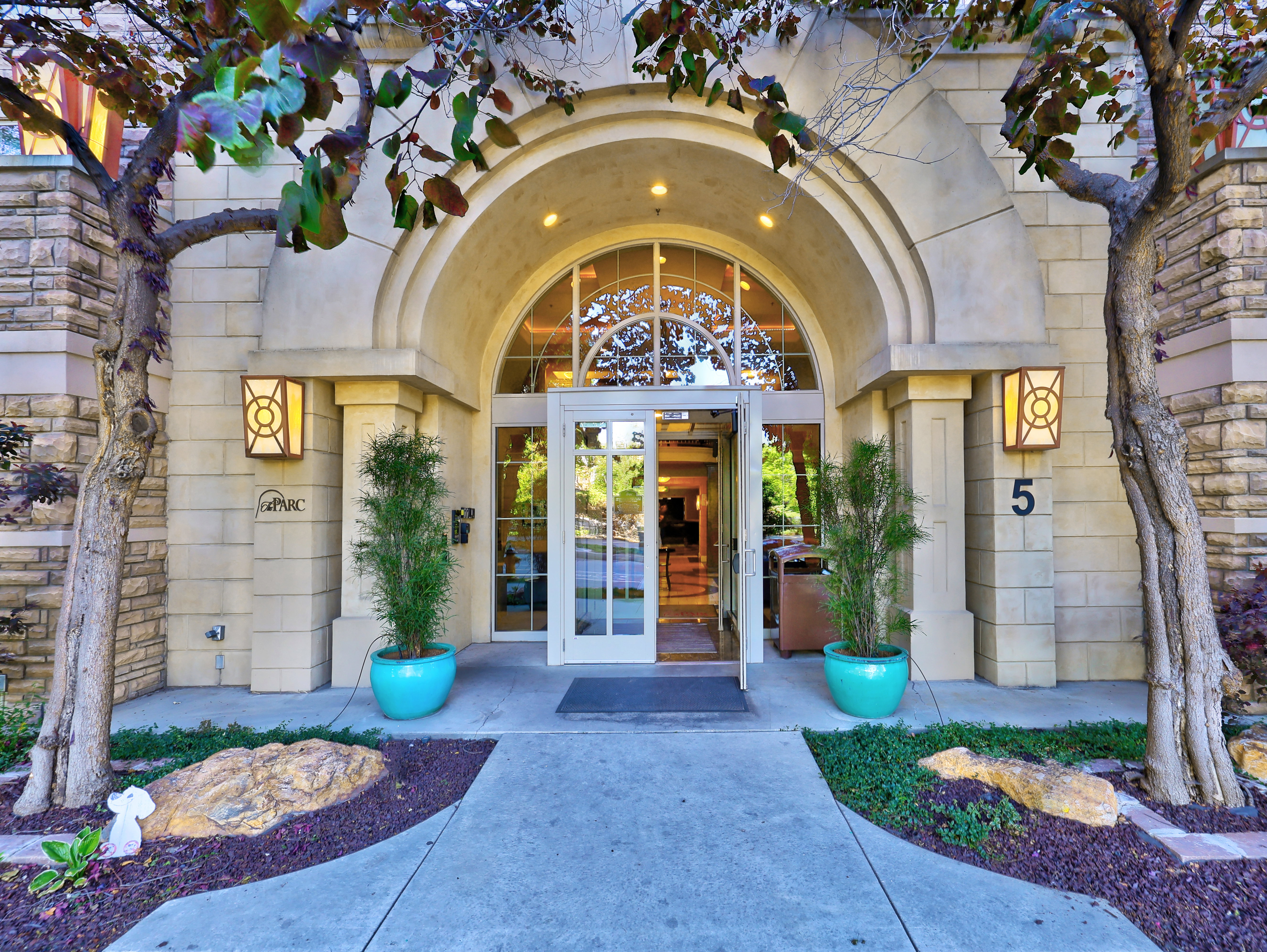 Arched entryway with transom window, flanked by stone veneer and decorative sconces