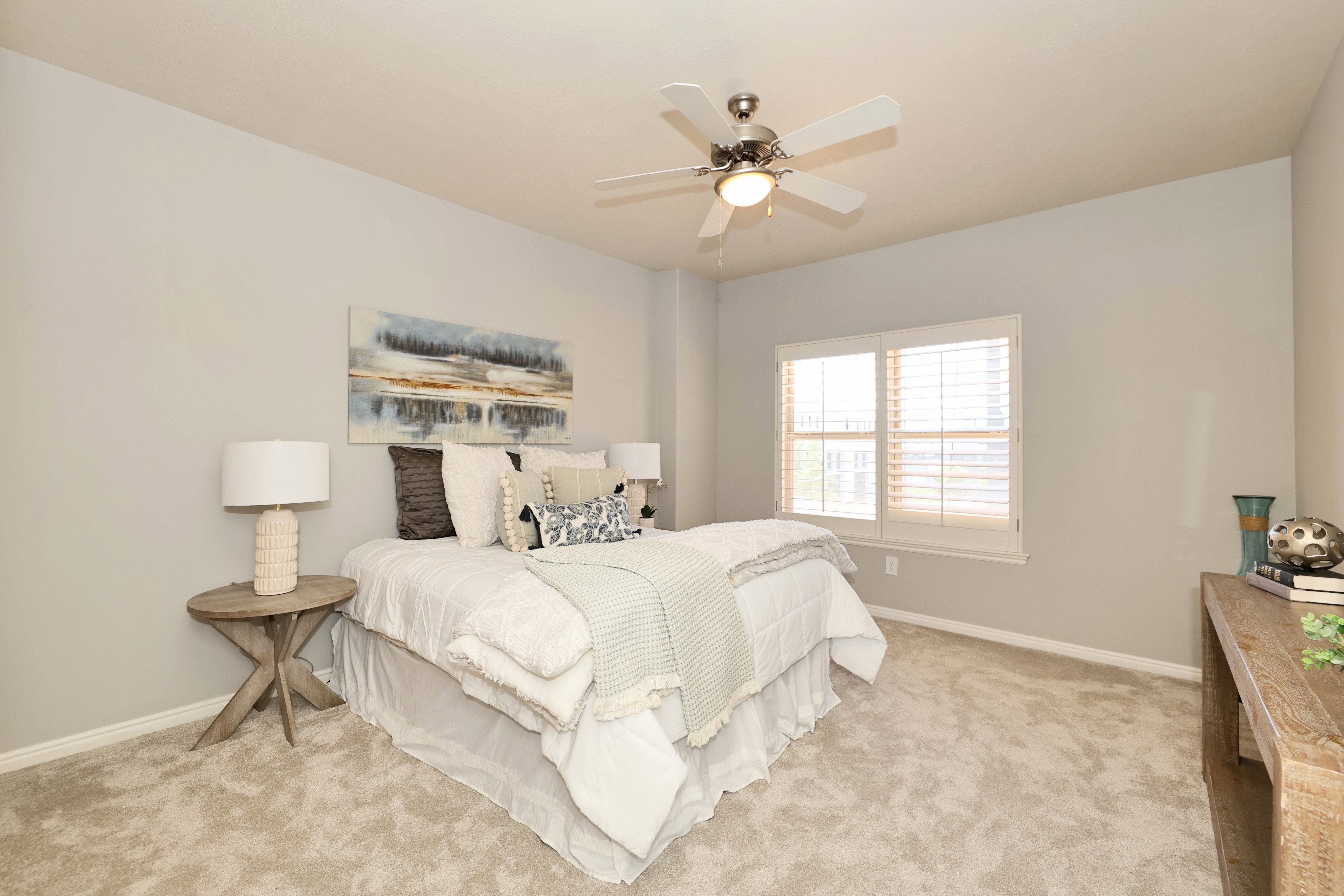 Carpeted bedroom featuring a ceiling fan with integrated lighting, a window with plantation shutters, a light gray wall color, and white baseboards
