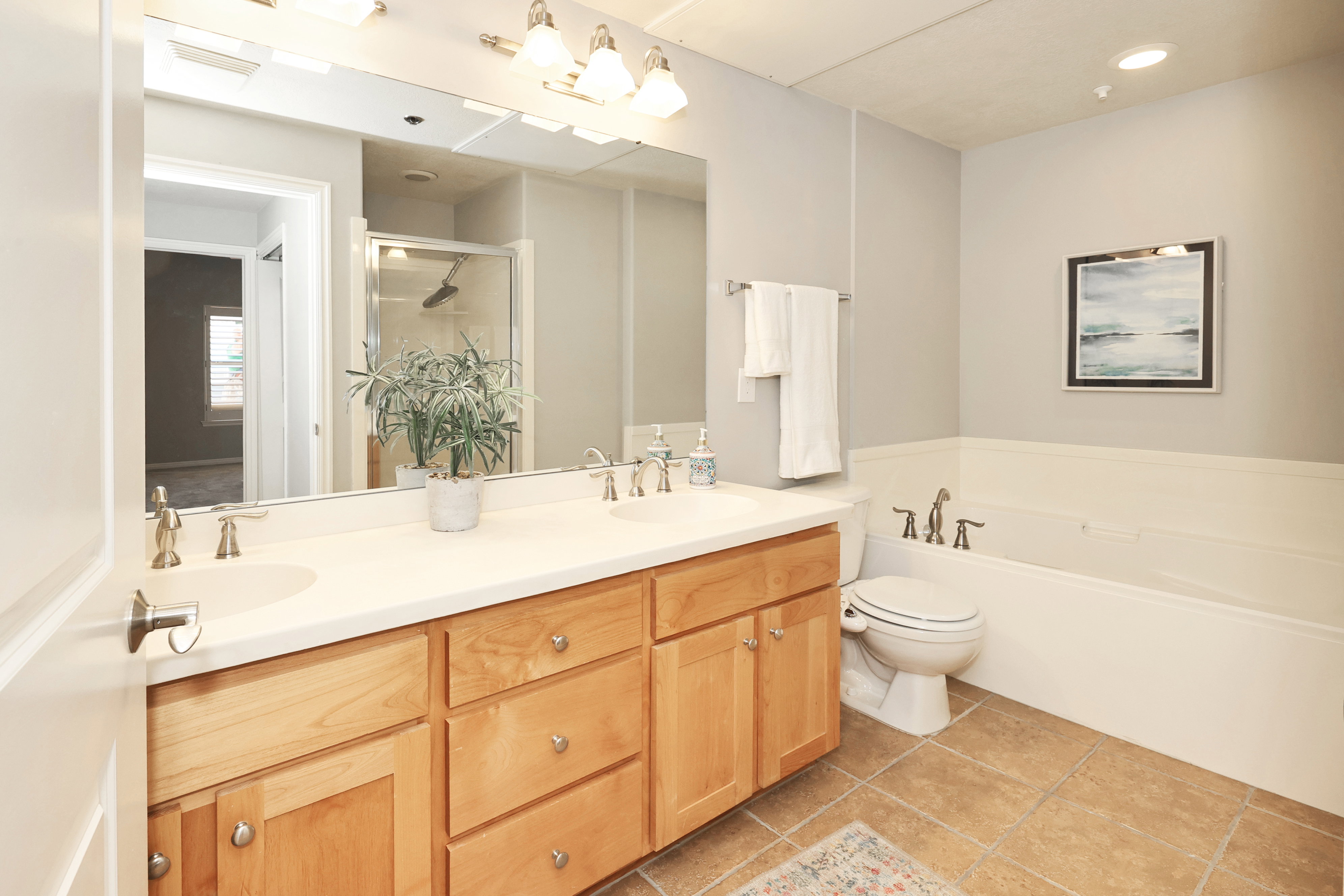 Bathroom featuring a double vanity with light wood cabinetry and dual sinks, a large wall-mounted mirror, a separate shower enclosure with a glass door, and a built-in bathtub with a white surround