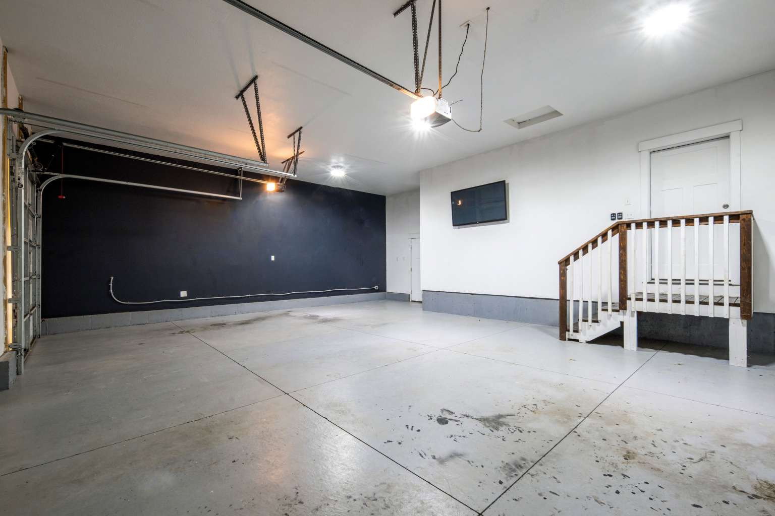 Spacious garage with concrete flooring, a partial black accent wall, and a built-in staircase with wood railings