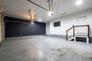 Spacious garage with concrete flooring, a partial black accent wall, and a built-in staircase with wood railings