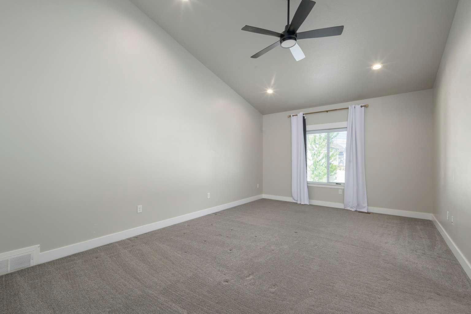 Spacious room featuring a vaulted ceiling with recessed lighting, a ceiling fan, light gray wall paint, and gray carpet flooring