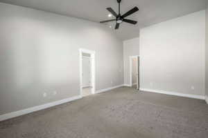 Spacious interior room featuring vaulted ceilings, neutral gray wall paint, dark carpet flooring, and a modern black ceiling fan