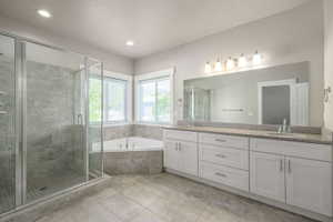 Spacious bathroom featuring a glass-enclosed shower with tiled walls, a corner soaking tub, dual vanity with granite countertops, and light-colored cabinetry