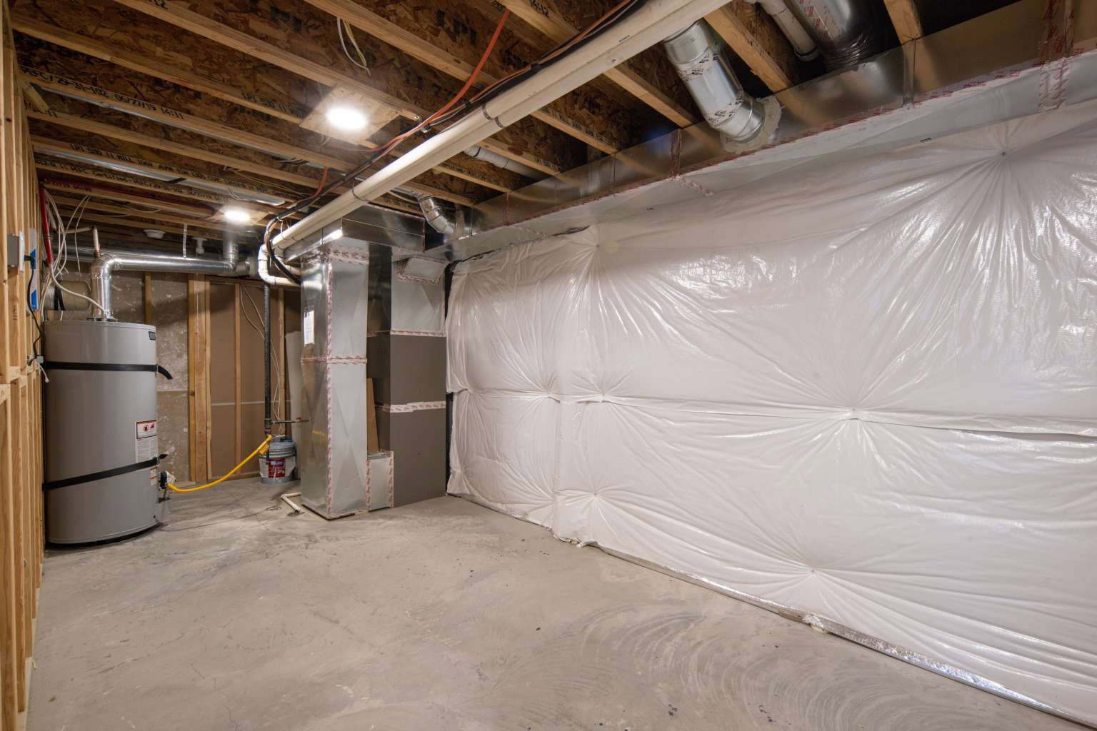 Unfinished basement featuring a concrete floor, exposed wood joists, utility systems, and insulated walls