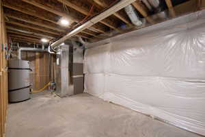 Unfinished basement featuring a concrete floor, exposed wood joists, utility systems, and insulated walls