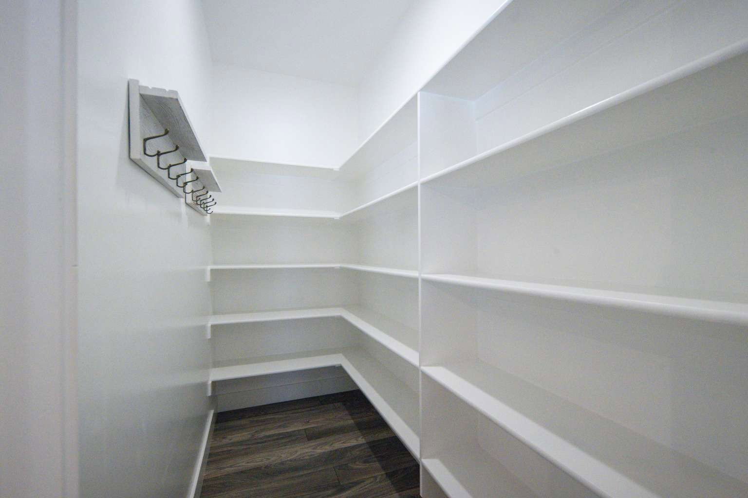 Walk-in pantry featuring extensive built-in shelving, wood-finish flooring, and a wall-mounted coat rack with multiple hooks