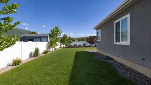 Expansive lawn area featuring a white privacy fence, landscaping rocks, and young trees