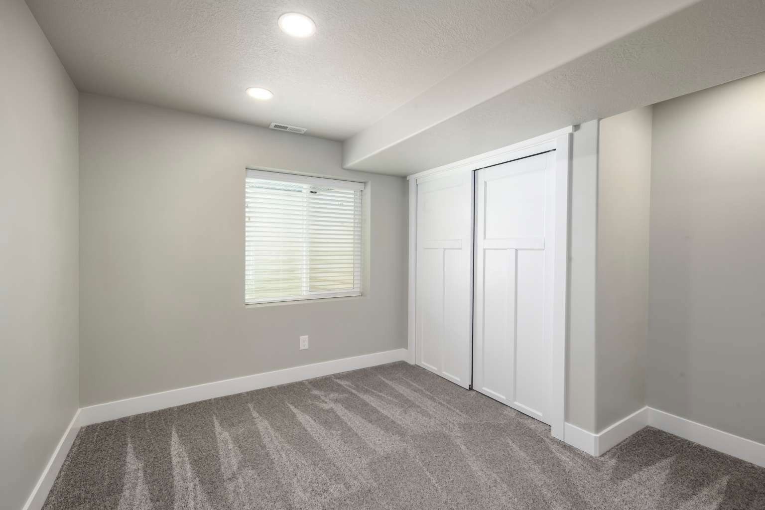 Room featuring gray carpeting, light gray walls, white baseboards, and a window with white horizontal blinds
