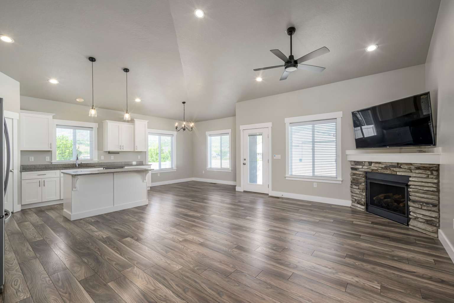 Spacious open concept living area featuring wood-finish flooring, a stone-clad fireplace, and vaulted ceilings with recessed lighting