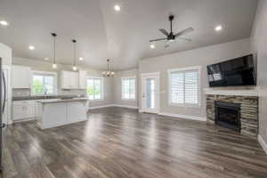 Spacious open concept living area featuring wood-finish flooring, a stone-clad fireplace, and vaulted ceilings with recessed lighting