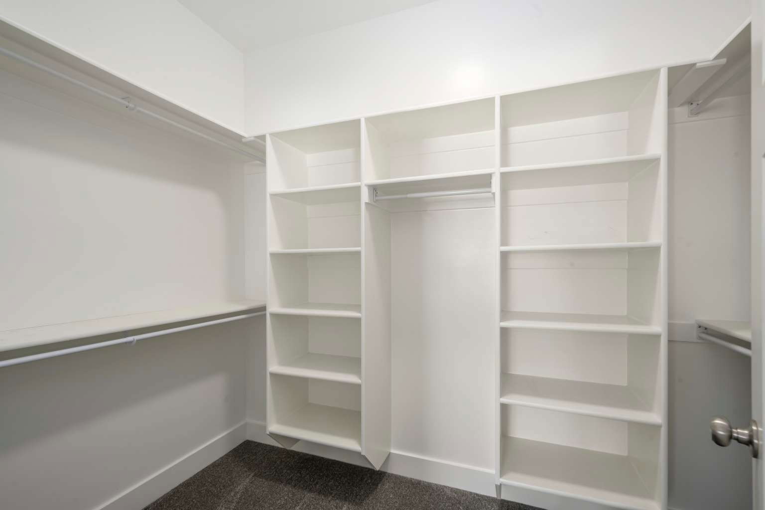 Walk-in closet featuring built-in shelving, white walls, dark gray carpet, and multiple hanging rods