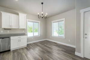 Open-concept area featuring wood-finish flooring, white shaker cabinetry, a stainless steel dishwasher, and a dark bronze chandelier