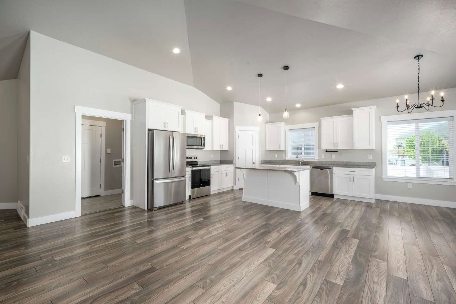 Open-concept kitchen and living area featuring wood-finish flooring, white cabinetry, a kitchen island, stainless steel appliances, and a vaulted ceiling with recessed lighting