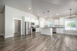 Open-concept kitchen and living area featuring wood-finish flooring, white cabinetry, a kitchen island, stainless steel appliances, and a vaulted ceiling with recessed lighting