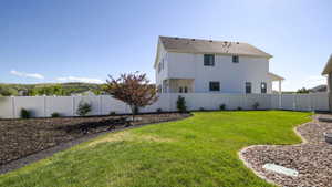 Expansive backyard featuring a manicured lawn, white privacy fencing, and landscaping beds with dark mulch