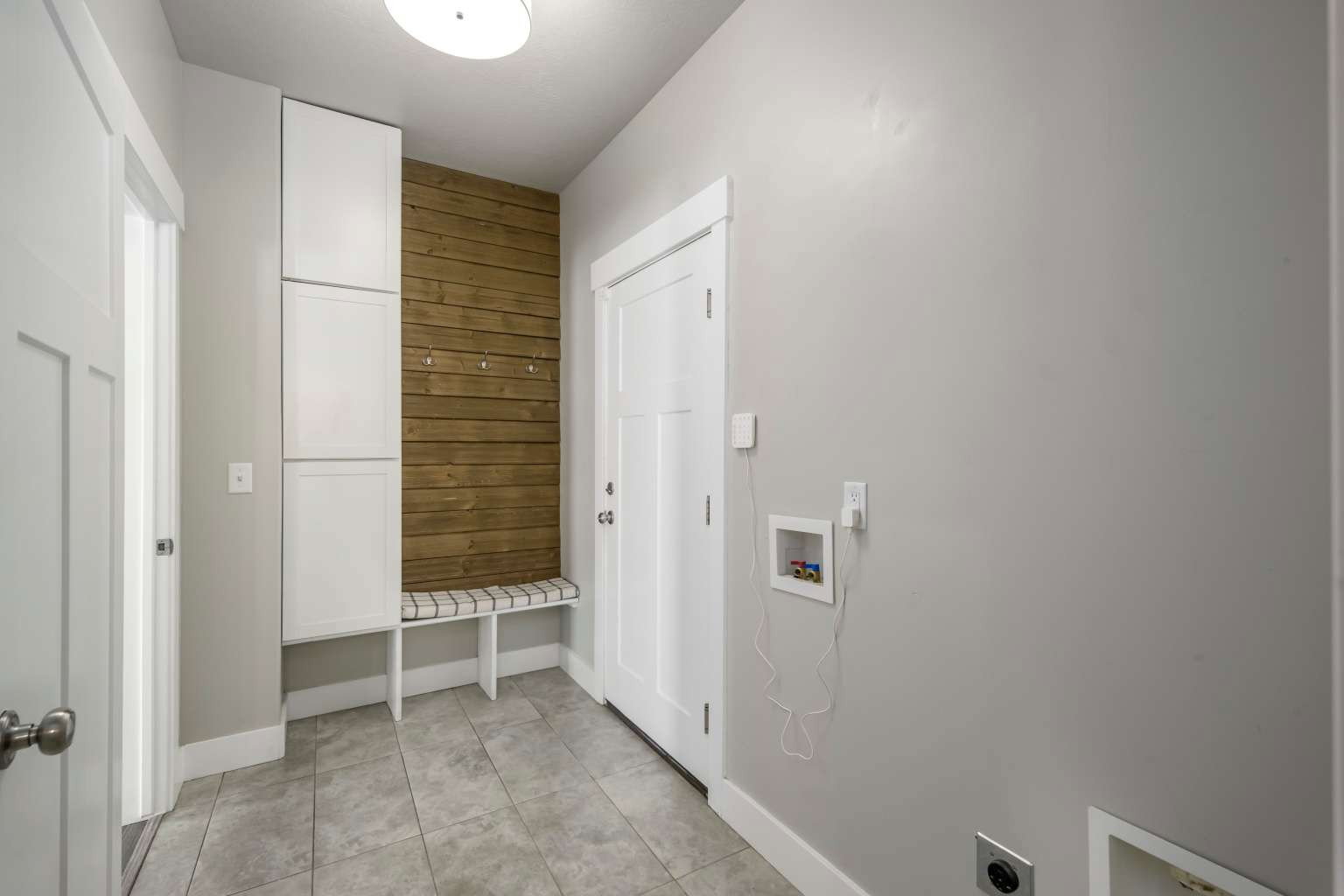 Utility area featuring a built-in bench with striped cushion, white panel cabinetry, and a wood-finish accent wall with hooks