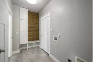 Utility area featuring a built-in bench with striped cushion, white panel cabinetry, and a wood-finish accent wall with hooks