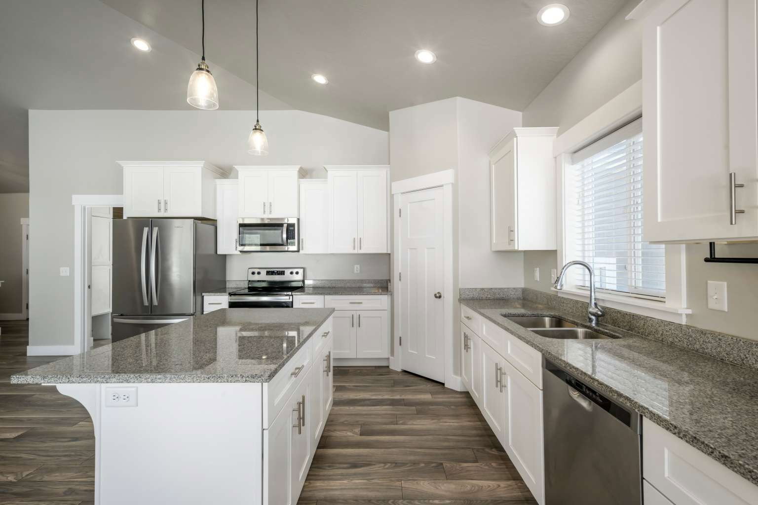 Kitchen featuring a central island with a granite countertop, white shaker cabinetry, stainless steel appliances, wood-finish flooring, and recessed lighting