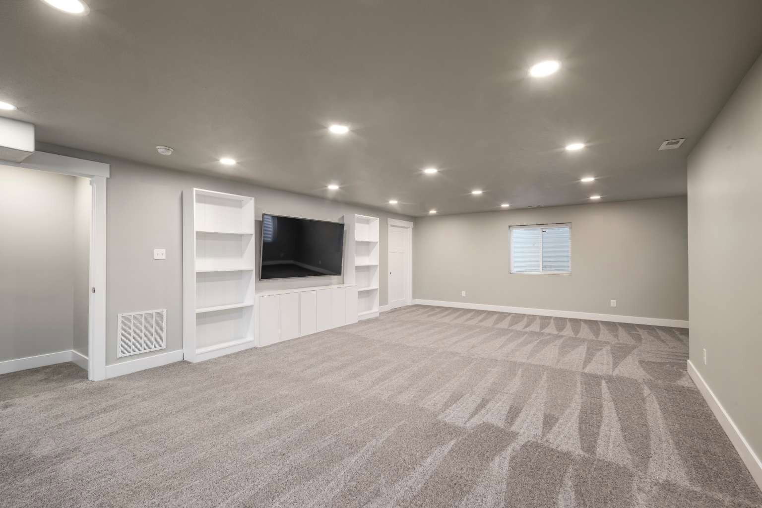 Spacious room featuring neutral carpeting, recessed lighting, and a built-in media center with shelving