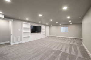Spacious room featuring neutral carpeting, recessed lighting, and a built-in media center with shelving