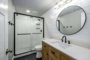 Modern bathroom featuring a glass-enclosed shower with subway tile, wood-finish vanity with a light-colored countertop, matte black hardware, and a round wall-mounted mirror