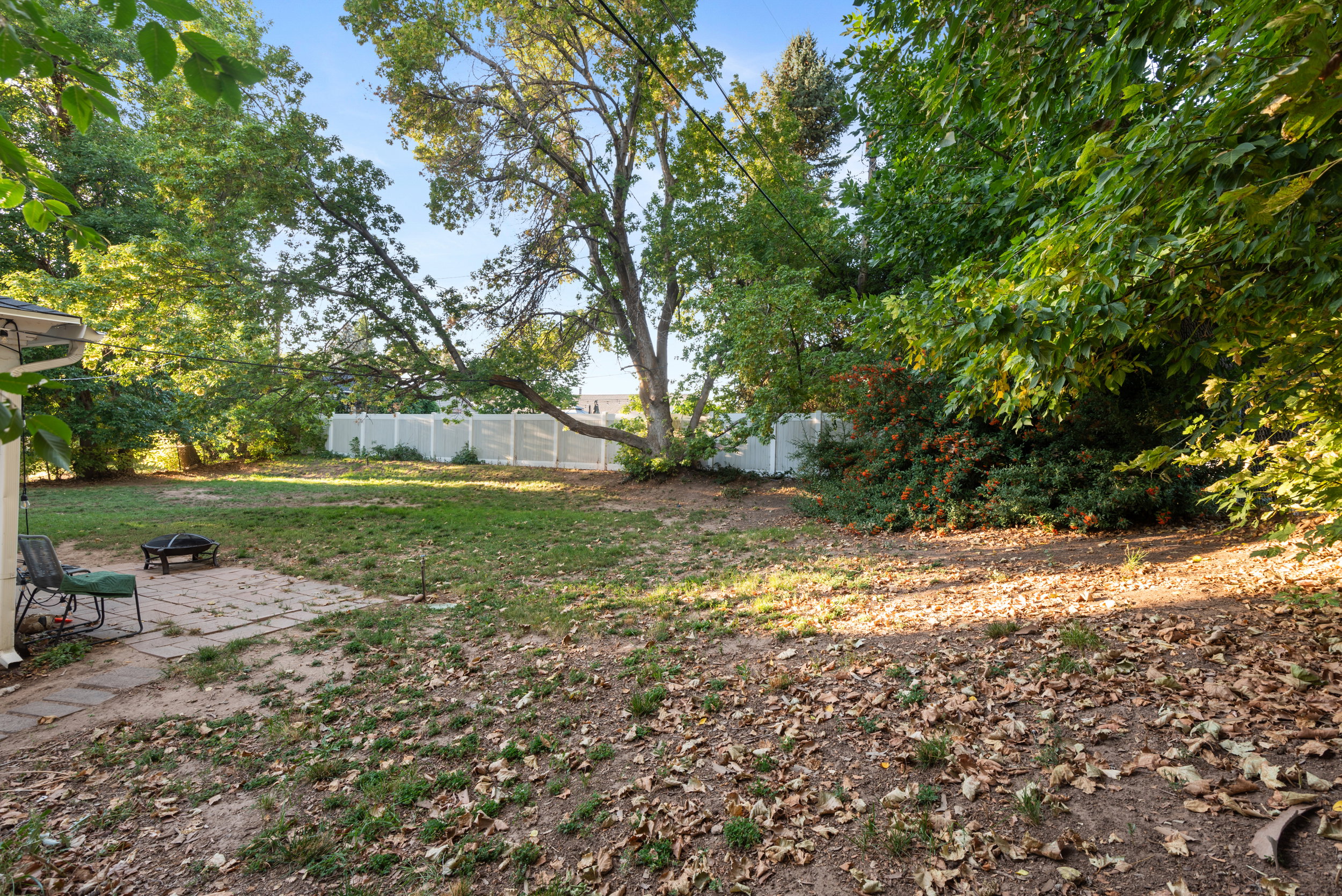 Expansive backyard featuring a partial stone patio, mature trees, and a white privacy fence