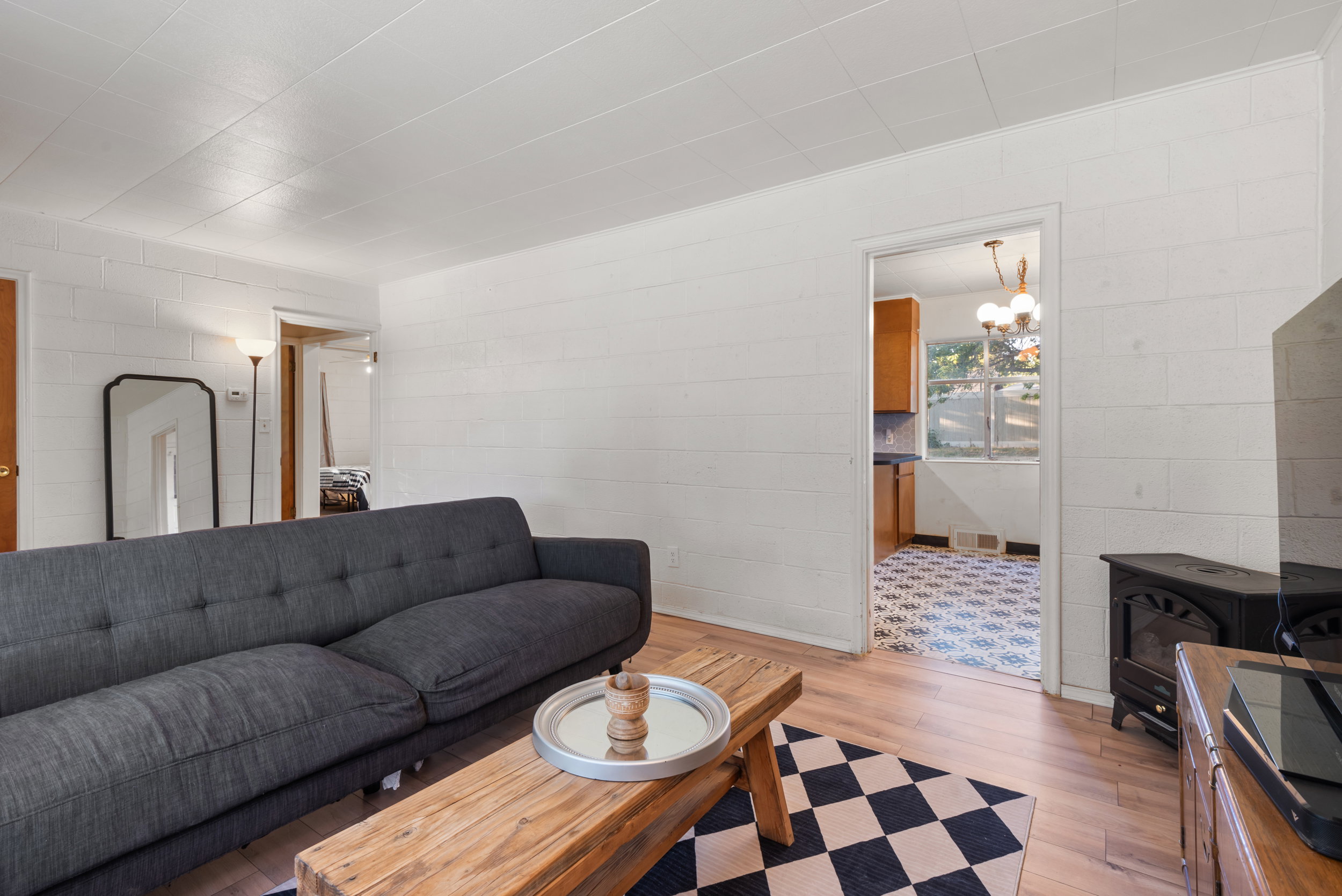 Living area with wood-finish flooring, white horizontal wall paneling, and an open doorway revealing a separate space with patterned tile flooring and a window