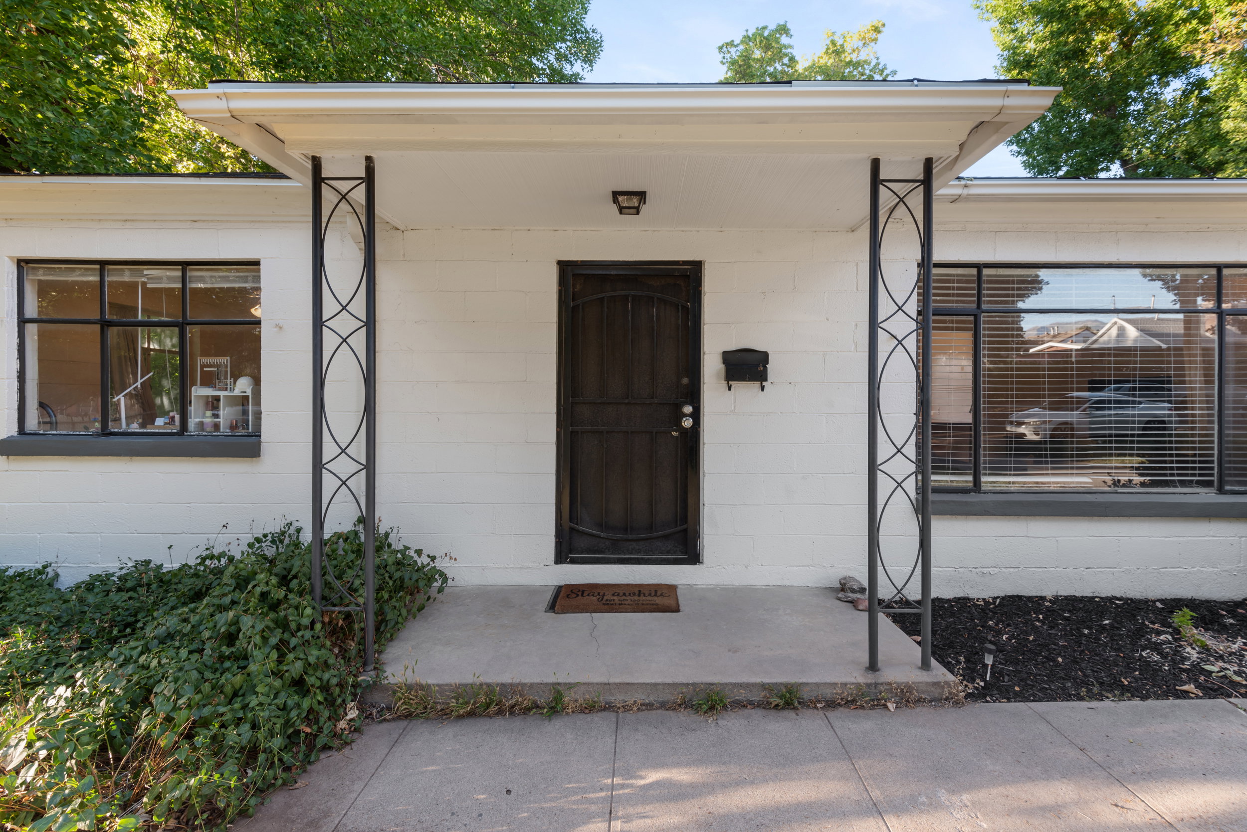 White exterior featuring a dark entry door, two decorative metal support columns, and large windows with black trim
